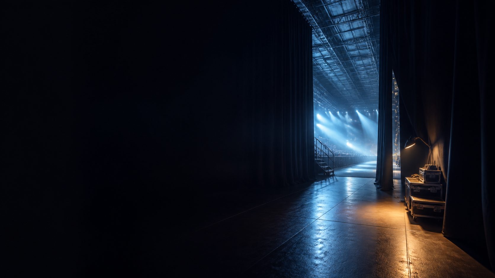 Backstage curtains opening toward a blue-lit stage, with production cases nearby