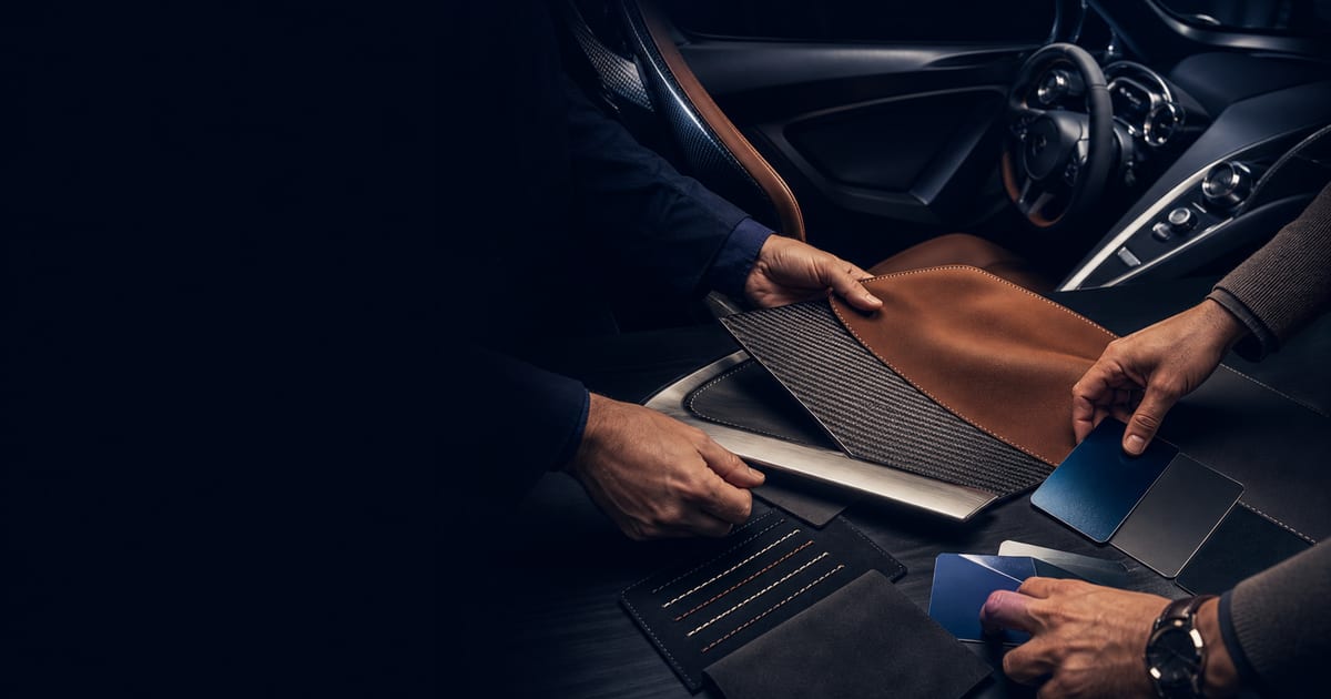 A client and automotive design specialist selecting leather, carbon fiber, stitching, metal, and paint finishes for a bespoke exotic car